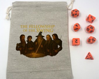 Puede incluir: Una bolsa beige con cordón con el texto "THE FELLOWSHIP OF THE SWING" y una ilustración de varias figuras. Junto a la bolsa hay varios dados naranjas con números blancos, incluyendo un D4, D6, D8, D10, D12 y D20.