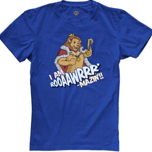 May include: Royal blue t-shirt featuring a cartoon lion wearing a crown and holding a medal. The lion is depicted with a red cape and a white fur collar. Text on the shirt reads "I AM ROOAAWRRR -MAZIN!!"