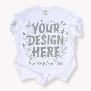 May include: White t-shirt with the text "YOUR DESIGN HERE" in gray, surrounded by decorative elements. The shirt is a mockup, perfect for showcasing custom designs. The words "Mockup Couture" are printed at the bottom of the design.
