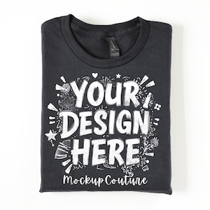 Puede incluir: Una camiseta negra doblada con las palabras blancas "YOUR DESIGN HERE", rodeadas de elementos decorativos. El texto "Mockup Couture" está impreso debajo. La camiseta está doblada.