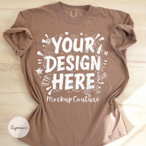 May include: Espresso-colored t-shirt with the text "YOUR DESIGN HERE" in a white, stylized font. The shirt is a mockup, with the words "Mockup Couture" below the main text. The shirt is folded on a light wood surface.