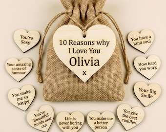 May include: A burlap gift bag with a drawstring closure, surrounded by wooden heart-shaped tokens. The large heart-shaped tag reads "10 Reasons why I Love You Olivia." Smaller hearts have phrases like "You're Sexy" and "Your Big Smile."