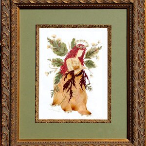 May include: A framed pressed flower art piece depicting a fairy with red hair and a floral crown. The fairy is wearing a dress made of dried leaves and flowers. The background is a green mat.
