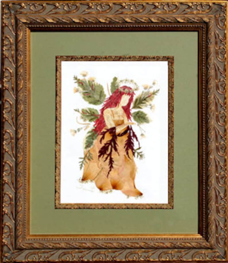 May include: A framed pressed flower art piece depicting a fairy with red hair and a floral crown. The fairy is wearing a dress made of dried leaves and flowers. The background is a green mat.