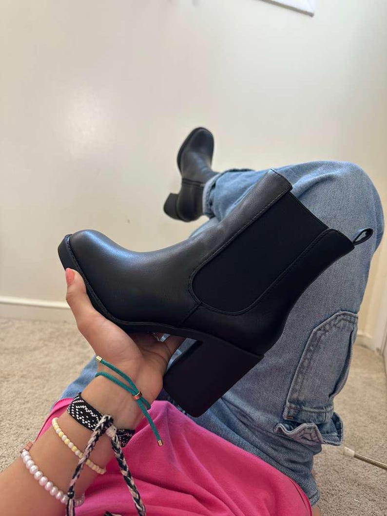 May include: Black ankle boots with a block heel. The boots have a smooth leather-like appearance and elastic side panels. The heel is approximately 3 inches high. The boots are shown with blue jeans and a pink top.