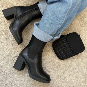 May include: Black leather ankle boots with block heels and a side zipper. The boots have a rounded toe and a platform sole. A small black square wallet with a grid pattern is next to the boots.