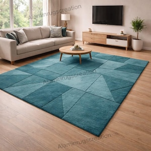 May include: A teal geometric patterned rug in a living room setting. The rug features various shades of teal arranged in a patchwork design. The rug is placed on a wooden floor, with a sofa, coffee table, and entertainment center in the background.
