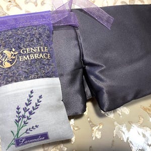 May include: A dark blue eye mask and a small sachet of lavender. The sachet is purple mesh filled with dried lavender buds and has the words "GENTLE EMBRACE" printed on it. A lavender sprig is embroidered on the white bottom of the sachet.