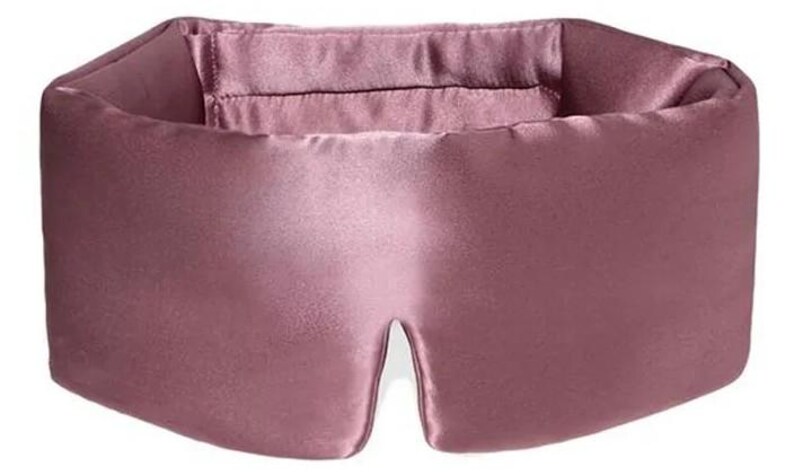 May include: A dusky pink sleep mask crafted from a silky fabric. The mask features a broad band for the head and a shaped eye area. The design is simple and elegant, suggesting a focus on comfort and light blockage for better sleep.