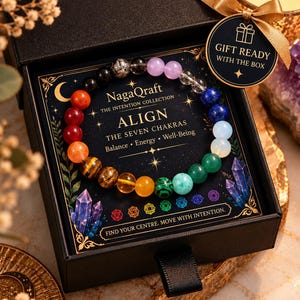 May include: A beaded bracelet featuring multi-colored stones arranged in a circular pattern inside a black gift box. The display card reads NagaQraft The Intention Collection Align The Seven Chakras Balance Energy Well-Being and Find Your Centre.