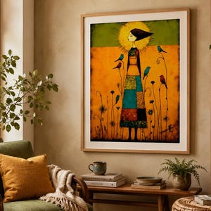 May include: A framed wall art print featuring a stylized figure with a golden halo standing in a field of tall, thin flowers. The figure wears a patchwork skirt in shades of blue, teal, and brown, surrounded by several small, colorful birds.