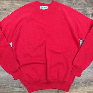 Könnte beinhalten: Ein leuchtend rotes Gap Sport Sweatshirt. Das Sweatshirt mit Rundhalsausschnitt hat lange Ärmel mit gerippten Bündchen und einem gerippten Saum. Auf dem Etikett am Halsausschnitt steht "GAP SPORT". Das Sweatshirt ist aus einem weichen, einfarbigen Material.