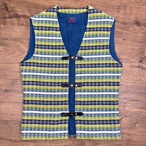 May include: A vintage vest with a geometric pattern in shades of green, blue, and white. The vest has a blue interior and fastens with three black leather straps. The Pendleton label is visible inside the vest.