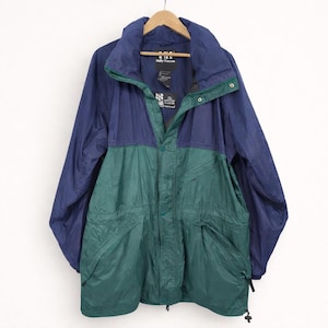 May include: A vintage Helly Hansen jacket in navy blue and green, hanging on a wooden hanger. The jacket has a collared neckline, a zipper closure, and two front pockets. The jacket has a tag that reads "Helly Hansen".