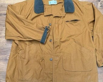 May include: A tan jacket with a dark teal collar and cuffs. The jacket has four front pockets, a button-up closure, and a small label on the collar. The jacket is made of a durable material.