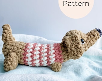 May include: A crocheted dachshund dog in tan and pink, wearing a pink and white striped sweater. The dog has black eyes and a black nose. The image includes the text "PDF Crochet Pattern" in a cream-colored oval.