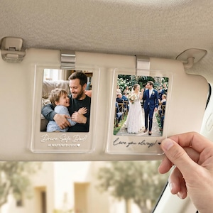 Op de afbeelding: Een auto zonnevizier met twee heldere acryl fotolijsten eraan geklikt. Elke lijst bevat een foto. Eén lijst heeft de tekst "Drive Safe Dad Always With You". De andere lijst heeft de tekst "Love you always!"