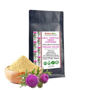 May include: A black packet of Balkanbio Milk Thistle Seed Powder, with text and a pink thistle design. A wooden bowl of powder and purple thistles are in front. The text reads "PREMIUM GRADE".