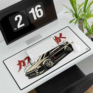 Pode incluir: Um tapete de secretária retangular com fundo branco e uma ilustração preta de um carro desportivo de perfil. O design inclui caracteres japoneses vermelhos e linhas de movimento estilizadas. O tapete tem uma borda preta e um pequeno logótipo.