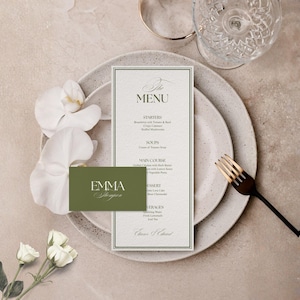 Op de afbeelding: Een trouwmenu en visitekaartje worden gepresenteerd op een bord met een vork met gouden punt en een glas. Het menu is wit met groene tekst en een groene rand. Het visitekaartje is olijfgroen met witte tekst.