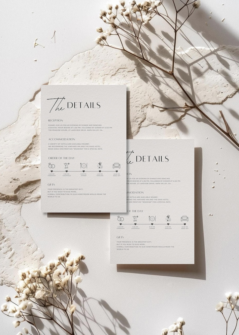 May include: Two ivory wedding detail cards with the text "The Details" in a minimalist font. The cards include information about the reception, accommodation, order of the day, and gifts. Delicate white flowers and branches are arranged around the cards.