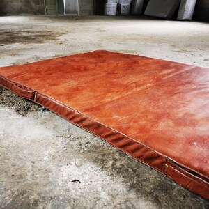Diagonal view of a handmade buffalo leather tatami laid flat on an industrial concrete floor. The natural texture and thick foam core create both comfort and visual impact. A statement piece for lofts, home gyms, or decorative interior styling.