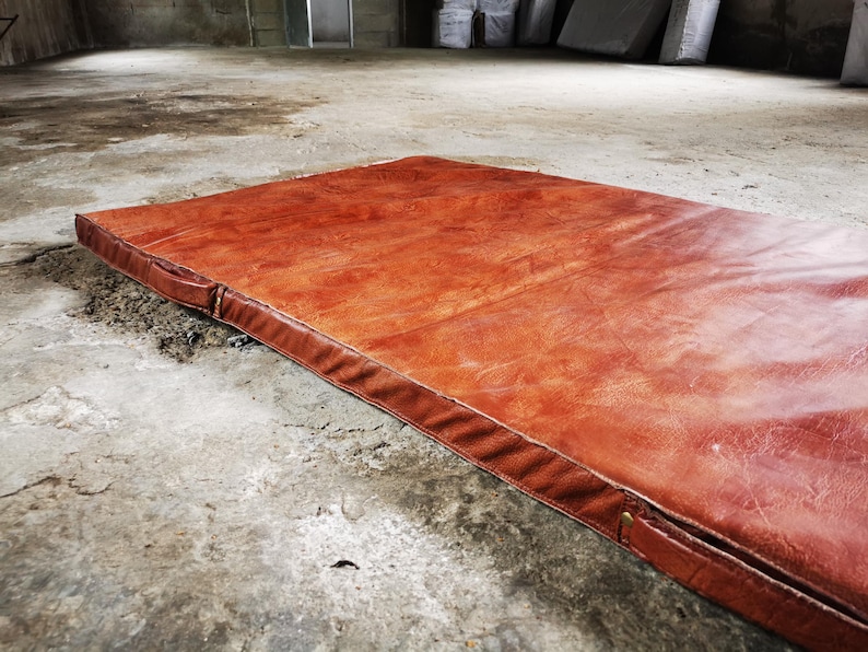 Diagonal view of a handmade buffalo leather tatami laid flat on an industrial concrete floor. The natural texture and thick foam core create both comfort and visual impact. A statement piece for lofts, home gyms, or decorative interior styling.