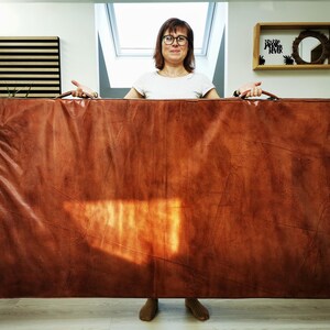 Full front view of a person holding the handmade buffalo leather mat vertically to show its real size. The large 180x100cm format, elegant patina, and soft foam interior make it suitable for yoga, relaxation, or stylish home decor with a vintage touch.