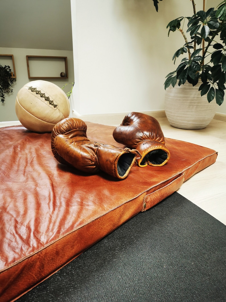 Lifestyle scene showing the vintage buffalo leather mat with old sports balls and gear beside it. The setup evokes nostalgic gym aesthetics, perfect for decorating studios, offices, or sports-themed interiors. Each Ben & Flo piece is unique and handcrafted in France.