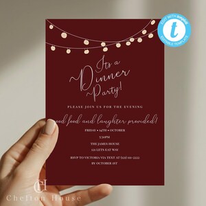 May include: Burgundy dinner party invitation with string lights and elegant script. Text includes "It's a Dinner Party!" and details for the event, such as date, time, and RSVP information. The invitation is held by a person.