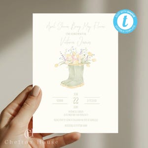 以下が含まれることがあります： 「April Showers Bring May Flowers」と「Come Shower Mom to Be」のテキストが入ったクリーム色の招待状。緑色の長靴に花が描かれた水彩イラストが特徴です。招待状にはイベントの詳細と「Edit with template」のテキストが含まれています。