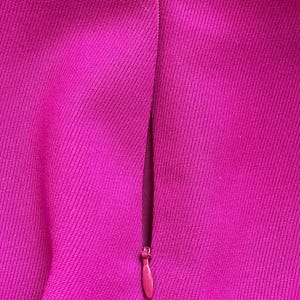May include: A vibrant magenta fabric surface featuring a concealed zipper closure. The textile has a distinct diagonal weave pattern, and the matching magenta zipper pull is positioned vertically along the seam of the garment material.