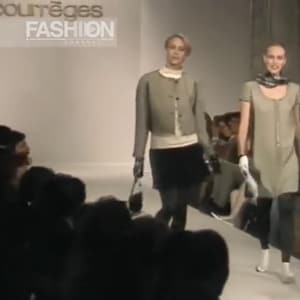 May include: Two models walking on a runway during a fashion show. The model on the left wears a light green jacket, black skirt, and carries a black purse. The model on the right wears a light green dress and carries a large bag. The text "courr&egrave;ges FASHION" is visible.