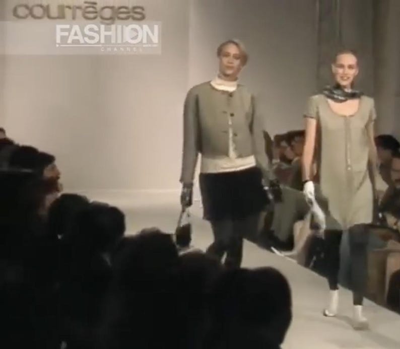 May include: Two models walking on a runway during a fashion show. The model on the left wears a light green jacket, black skirt, and carries a black purse. The model on the right wears a light green dress and carries a large bag. The text "courr&egrave;ges FASHION" is visible.