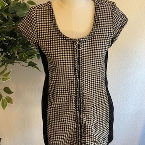 May include: A black and white checkered dress with a scoop neckline and short sleeves. The dress features a full-length zipper down the front and black side panels. The dress is displayed on a mannequin.