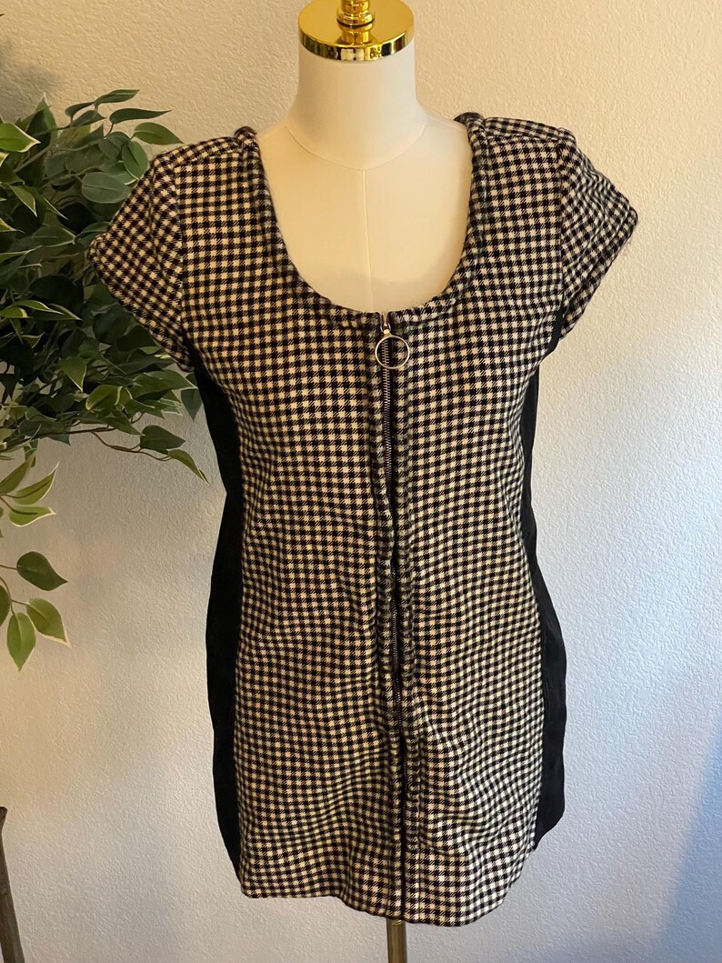 May include: A black and white checkered dress with a scoop neckline and short sleeves. The dress features a full-length zipper down the front and black side panels. The dress is displayed on a mannequin.