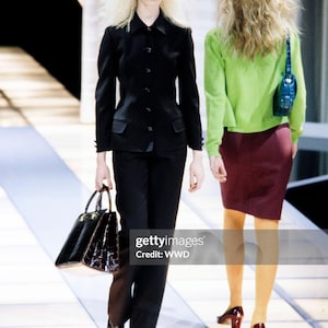 May include: A black tailored jacket and matching trousers paired with a dark brown textured handbag. Beside it, a lime green long-sleeved top, a dark maroon knee-length skirt, a small blue shoulder bag, and dark red block-heeled shoes.