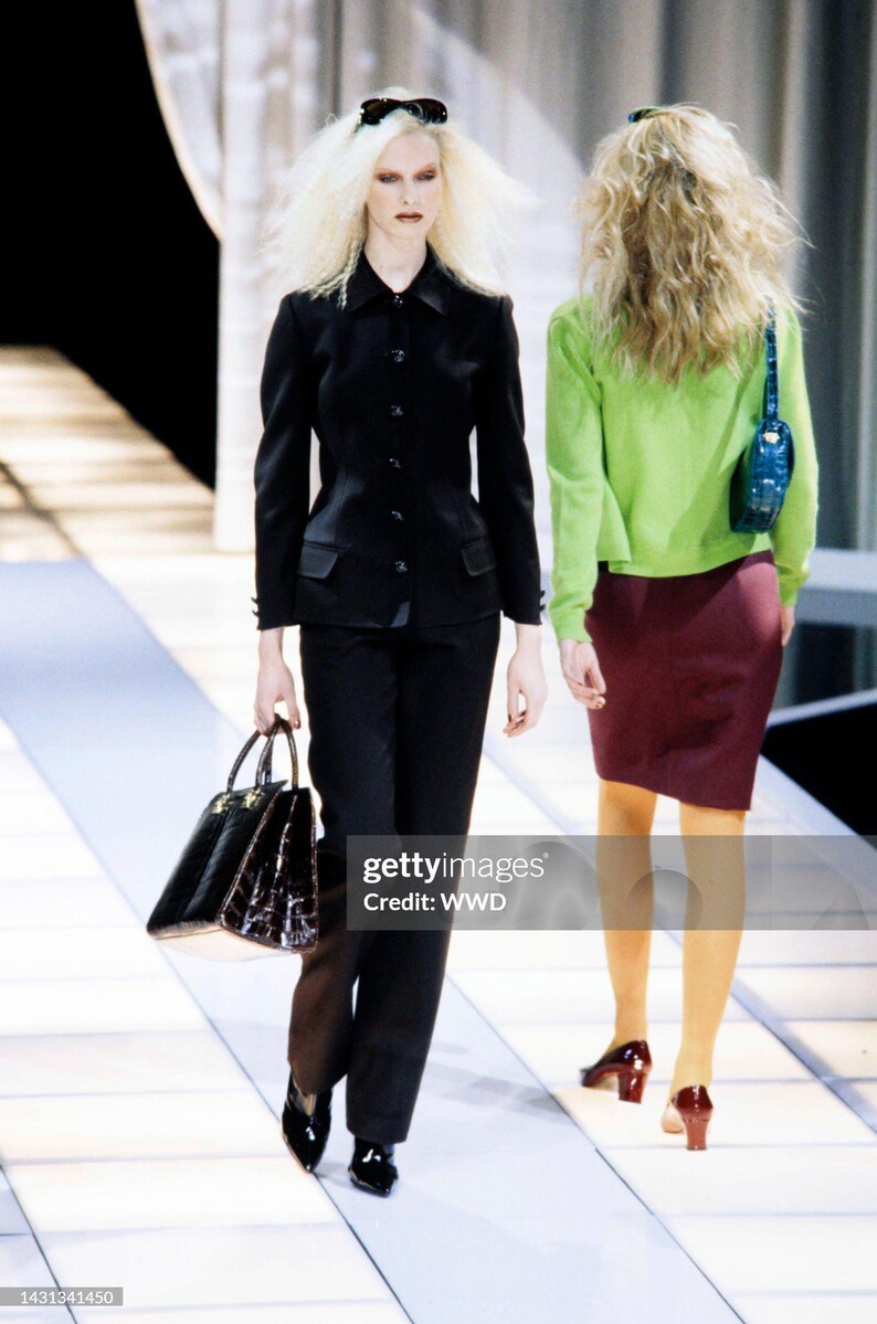 May include: A black tailored jacket and matching trousers paired with a dark brown textured handbag. Beside it, a lime green long-sleeved top, a dark maroon knee-length skirt, a small blue shoulder bag, and dark red block-heeled shoes.
