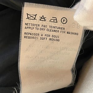 May include: A close-up of a clothing care label with text in French and English. The label includes symbols for washing, drying, and ironing instructions. The text reads "APPLY TO DRY CLEANER FOR WASHING" and "REQUIRES SOFT IRONING".