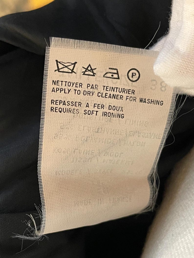 May include: A close-up of a clothing care label with text in French and English. The label includes symbols for washing, drying, and ironing instructions. The text reads "APPLY TO DRY CLEANER FOR WASHING" and "REQUIRES SOFT IRONING".