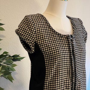 May include: A black and white checkered dress with a square neckline and short sleeves. The dress features a full-length zipper and a solid black panel on the side. The dress is displayed on a mannequin.