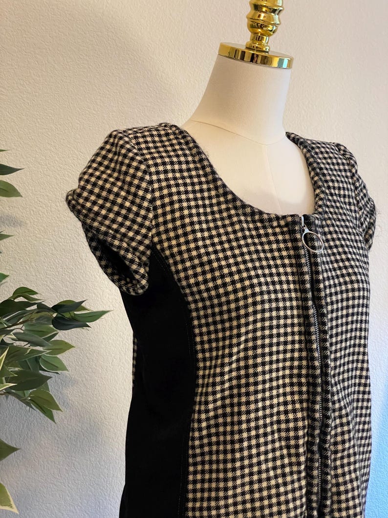 May include: A black and white checkered dress with a square neckline and short sleeves. The dress features a full-length zipper and a solid black panel on the side. The dress is displayed on a mannequin.