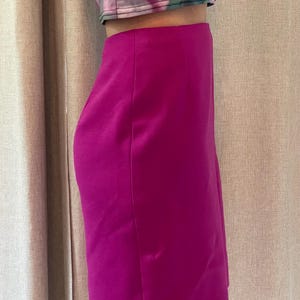 May include: A vibrant magenta knee-length skirt with a smooth, solid-colored finish and a clean, straight-cut silhouette. The skirt features a high-waisted design and is paired with a cropped top featuring a green and pink floral pattern.