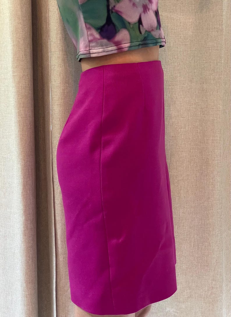 May include: A vibrant magenta knee-length skirt with a smooth, solid-colored finish and a clean, straight-cut silhouette. The skirt features a high-waisted design and is paired with a cropped top featuring a green and pink floral pattern.
