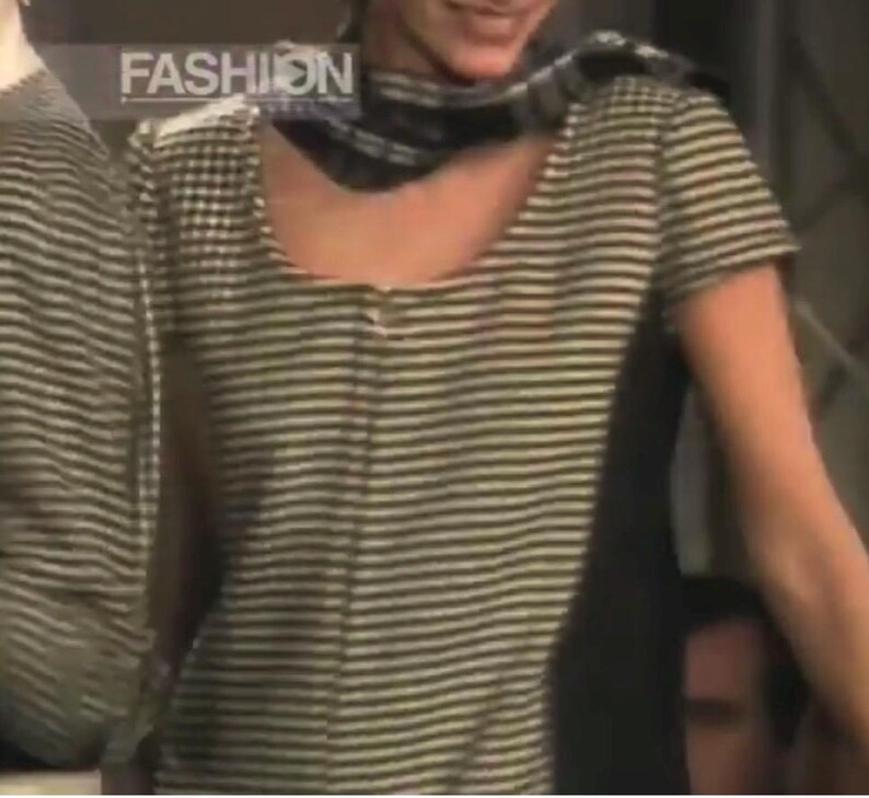 May include: A short-sleeved, striped shirt with a scoop neck. The shirt has horizontal stripes in shades of gray and white. The word "FASHION" is visible in the upper left corner. The shirt is part of a fashion collection.