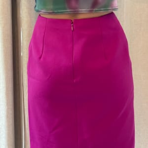 May include: A solid magenta mini skirt featuring a high-waisted design with a centered vertical zipper closure at the top. The skirt has a smooth, matte texture and a straight-cut silhouette that ends above the knee, paired with a cropped top.