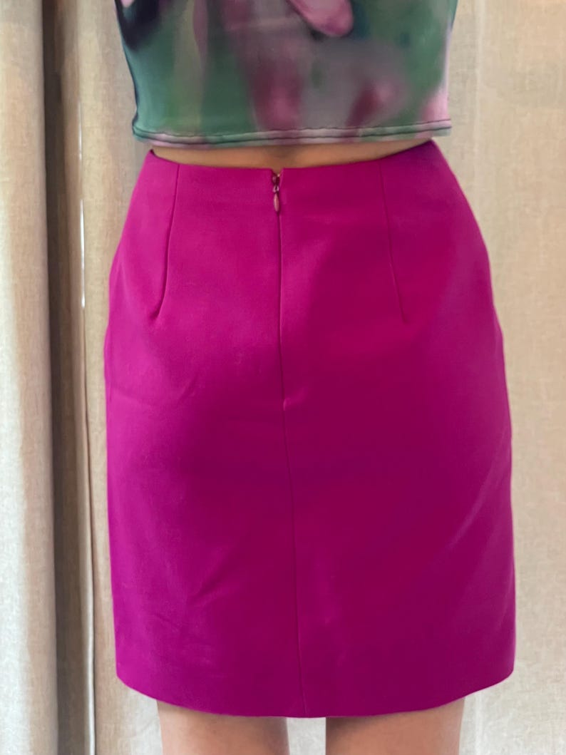 May include: A solid magenta mini skirt featuring a high-waisted design with a centered vertical zipper closure at the top. The skirt has a smooth, matte texture and a straight-cut silhouette that ends above the knee, paired with a cropped top.