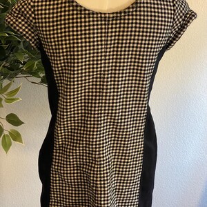 May include: A short-sleeved dress with a black and white checkered pattern on the front and back. The sides of the dress are solid black. The dress is displayed on a mannequin.