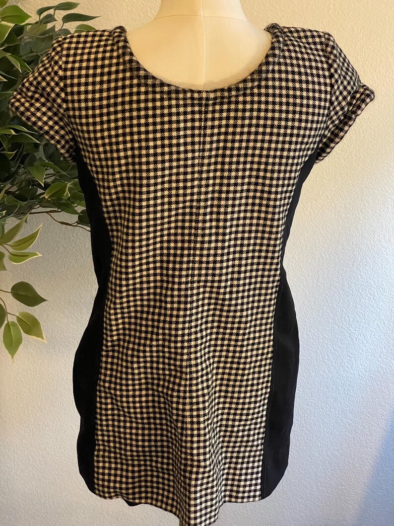 May include: A short-sleeved dress with a black and white checkered pattern on the front and back. The sides of the dress are solid black. The dress is displayed on a mannequin.