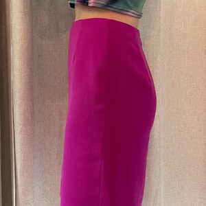 May include: A high-waisted, knee-length pencil skirt in a vibrant magenta pink color. The skirt features a smooth, solid fabric construction with a clean, straight silhouette and a subtle side seam detail, ending just above the knee.